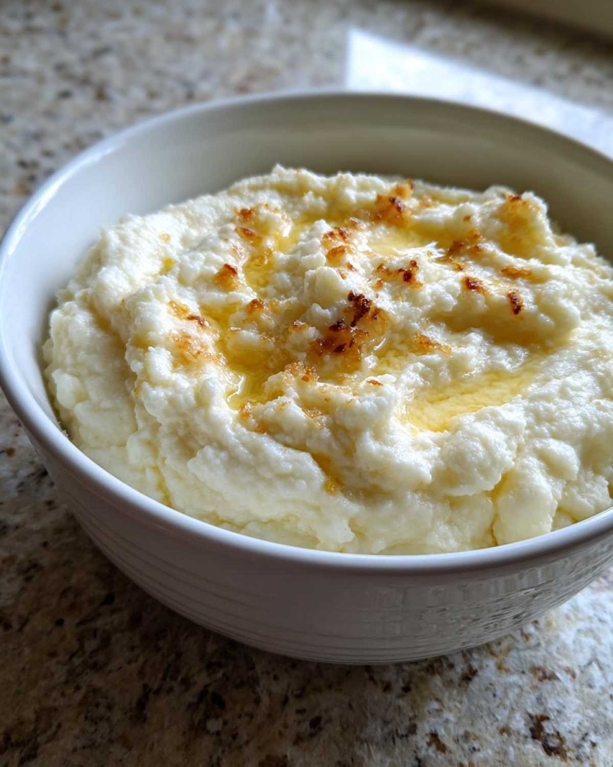 A white bowl filled with fluffy Creamy Garlic Mashed Cauliflower, topped with melted butter and browned bits.