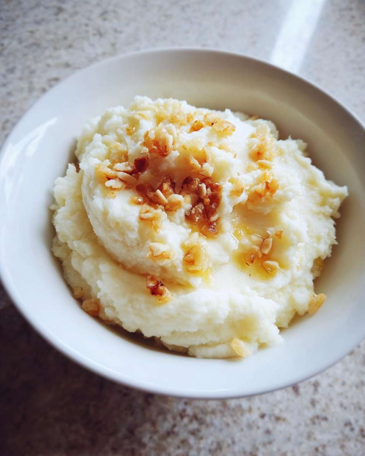 A white bowl filled with fluffy Creamy Garlic Mashed Cauliflower topped with browned garlic bits.