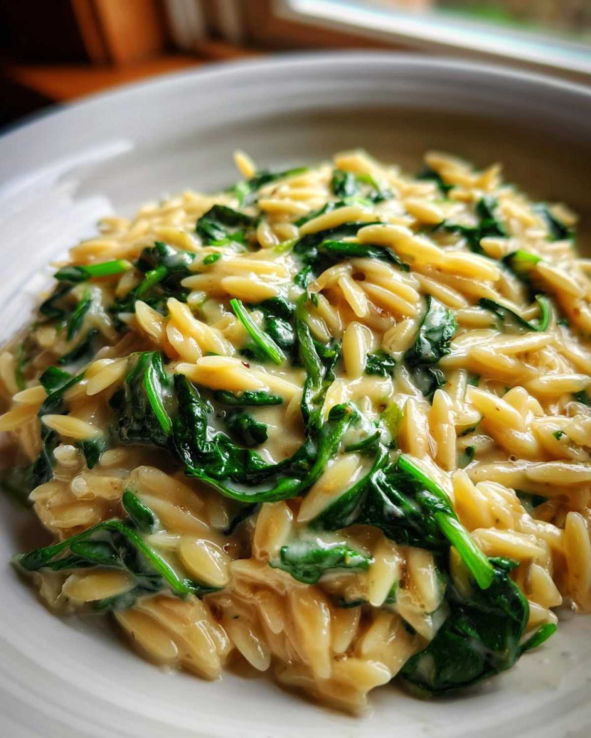 Close-up of a bowl filled with Creamy Garlic Parmesan Orzo with Spinach, showing rich sauce coating the pasta and wilted greens.