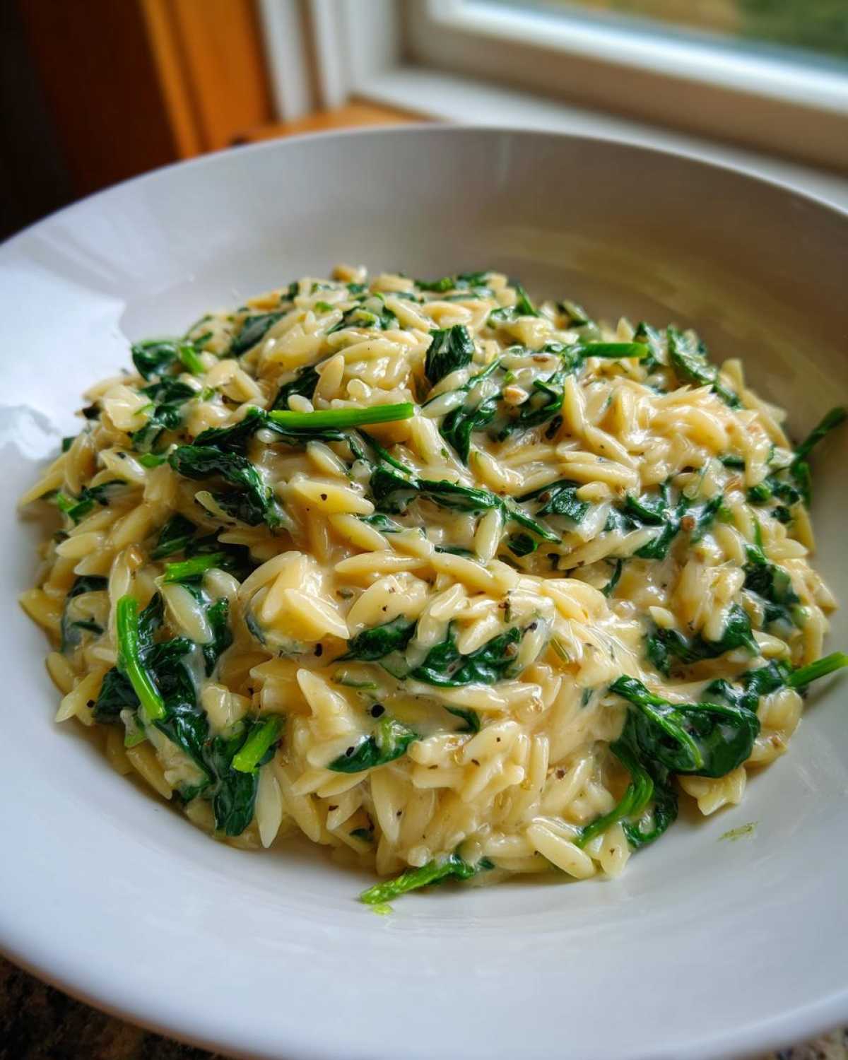 Close-up of a white bowl filled with creamy Garlic Parmesan Orzo with Spinach.