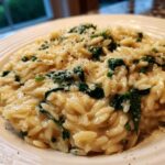A close-up shot of a serving of Creamy Garlic Parmesan Orzo with Spinach topped with grated cheese and black pepper.