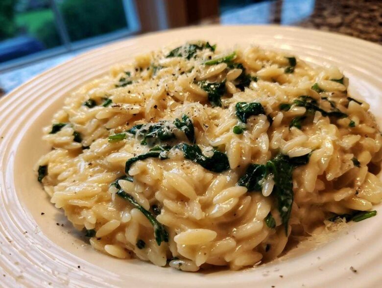 A close-up shot of a serving of Creamy Garlic Parmesan Orzo with Spinach topped with grated cheese and black pepper.