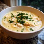 A close-up of a bowl of creamy Greek Lemon Chicken Soup with shredded chicken and orzo, topped with fresh parsley.