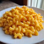 Close-up of a generous serving of creamy, bright orange Instant Pot Mac and Cheese on a white plate.