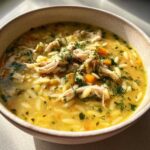 Close-up of a bowl of Creamy Lemon Chicken Orzo Soup, featuring shredded chicken, orzo pasta, carrots, and fresh dill.