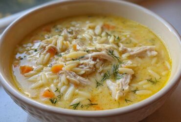 Close-up of a bowl filled with rich, yellow Creamy Lemon Chicken Orzo Soup, featuring shredded chicken, orzo pasta, and dill.