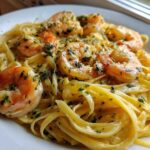 Close-up of a serving of Creamy Lemon Garlic Shrimp Pasta featuring fettuccine noodles and large, seasoned shrimp.