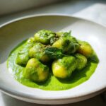 Close-up of bright yellow gnocchi coated in vibrant green creamy pesto sauce, served in a light bowl.