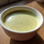 A close-up of smooth, light green Creamy Potato Leek Soup served in a white bowl on a wooden surface.
