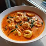 Close-up of a white bowl filled with rich Creamy Tomato Tortellini Soup, featuring tortellini pasta and wilted spinach.