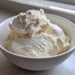 A white bowl filled with thick, creamy vanilla protein smoothie bowl mixture, resembling soft-serve ice cream.
