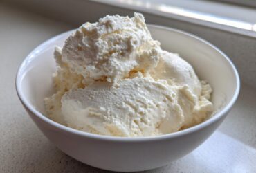 A white bowl filled with thick, creamy vanilla protein smoothie bowl mixture, resembling soft-serve ice cream.