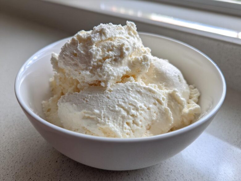 A white bowl filled with thick, creamy vanilla protein smoothie bowl mixture, resembling soft-serve ice cream.