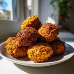 A stack of golden brown, crispy air fryer falafel piled high on a small white plate, backlit by a window.