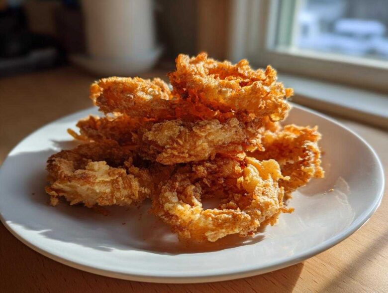 A close-up of a pile of golden brown, super crispy Air Fryer Onion Rings stacked on a white plate.