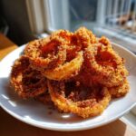A close-up of a generous serving of golden brown, crispy Air Fryer Onion Rings piled high on a white plate.