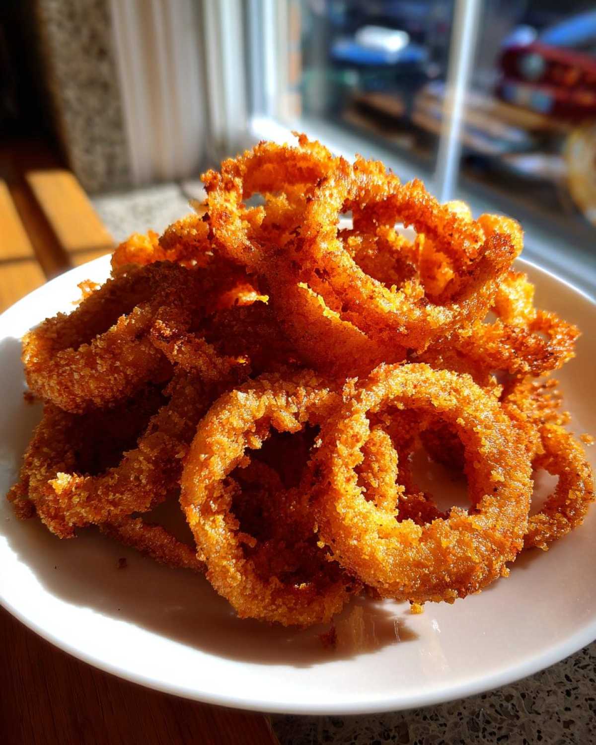 A close-up photo of a large pile of golden brown, crispy Air Fryer Onion Rings served on a white plate.