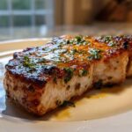 Close-up of a thick, juicy Crispy Air Fryer Pork Chop topped with glistening garlic butter sauce and fresh parsley.