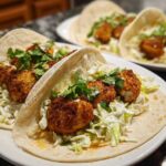 Two Crispy Baked Fish Tacos filled with golden breaded fish, lime slaw, and cilantro on a white plate.