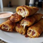 Stack of Crispy Baked Reuben Egg Rolls showing melted cheese and corned beef filling, served with Thousand Island Dip.