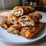 A stack of halved, crispy baked Reuben egg rolls showing melted cheese and filling, served with Thousand Island dip.