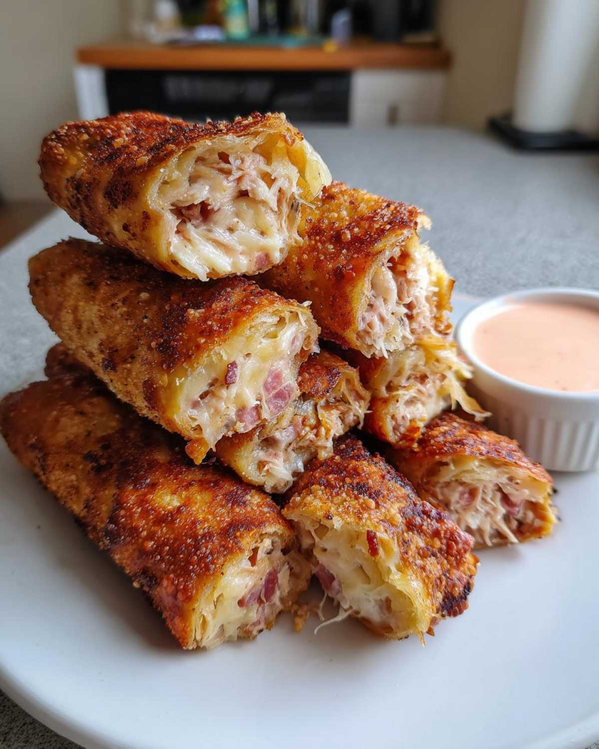 A stack of golden brown, crispy baked Reuben egg rolls cut open to show corned beef and cheese filling, served with Thousand Island Dip.