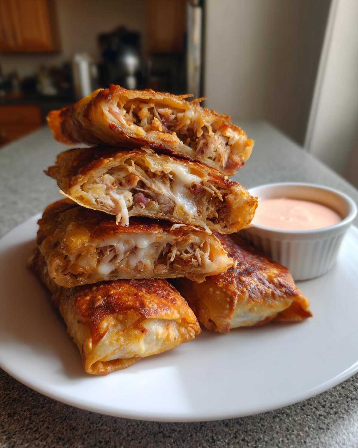 A stack of four Crispy Baked Reuben Egg Rolls, cut open to show melted cheese and filling, served with Thousand Island Dip.