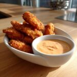 Crispy fried chicken tenders served with a side of creamy Copycat Raising Cane’s Sauce in a white dish.