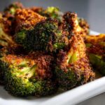Close-up of vibrant green broccoli florets heavily coated in a dark, crispy Parmesan crust.