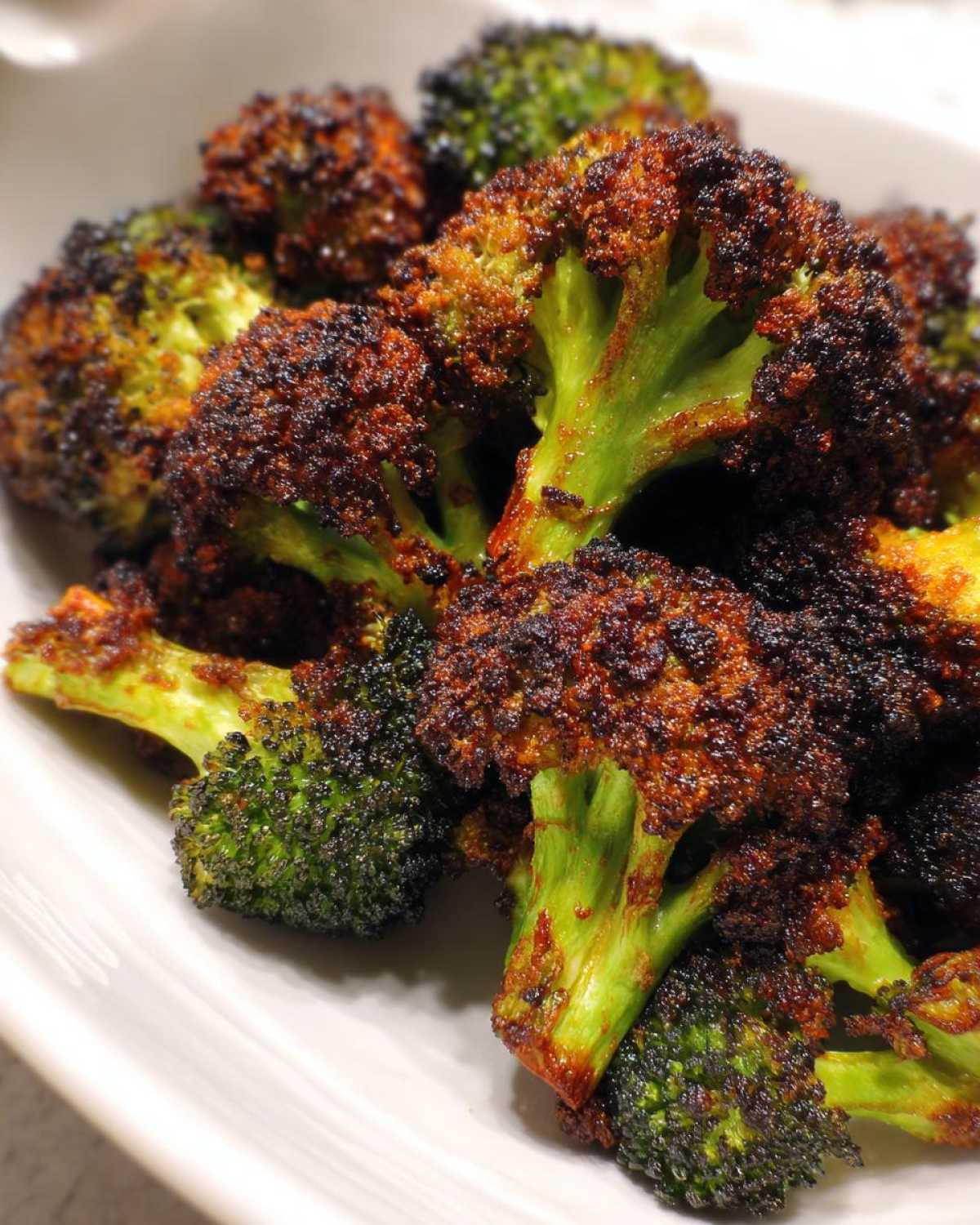 Close-up of intensely roasted broccoli florets showing dark, crispy parmesan coating and bright green stems, showcasing Crispy Parmesan Roasted Broccoli.