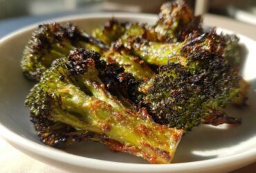 Close-up of perfectly charred and crispy Parmesan roasted broccoli florets served in a white bowl.