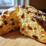 A golden-brown loaf of Easy Irish Soda Bread with Buttermilk and Raisins, cut in half to show the soft interior dotted with raisins.