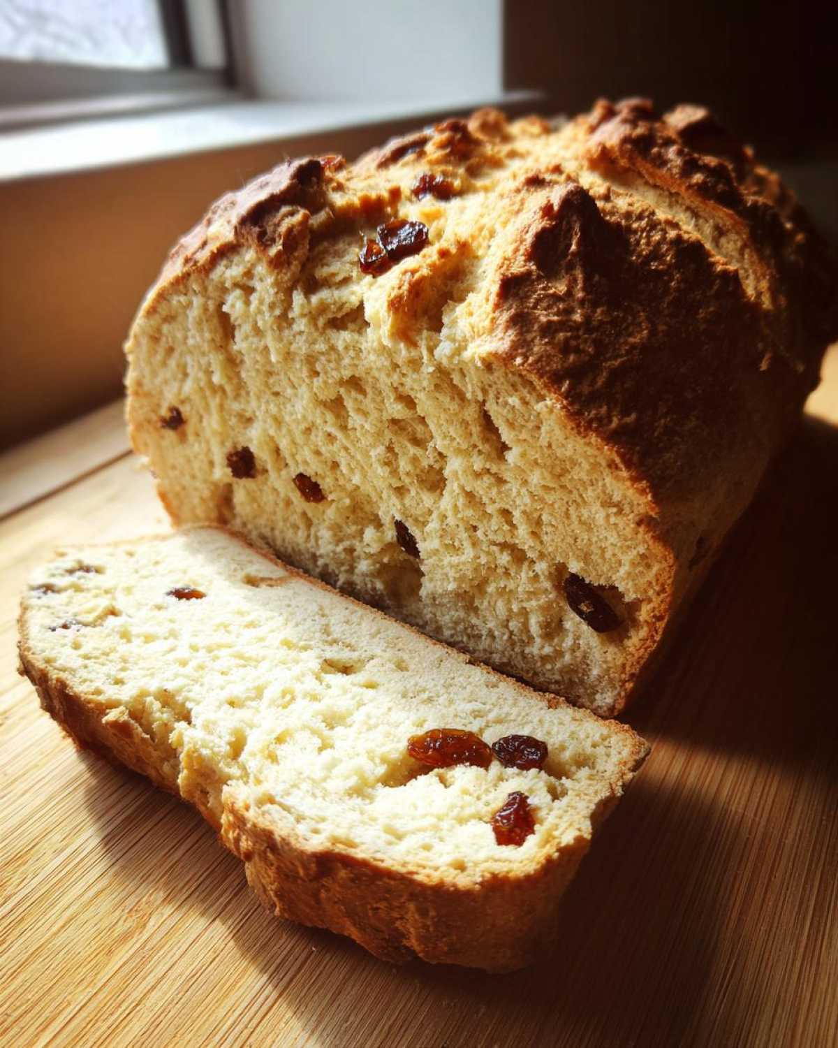 A loaf of Easy Irish Soda Bread with Buttermilk and Raisins, sliced open on a wooden board.