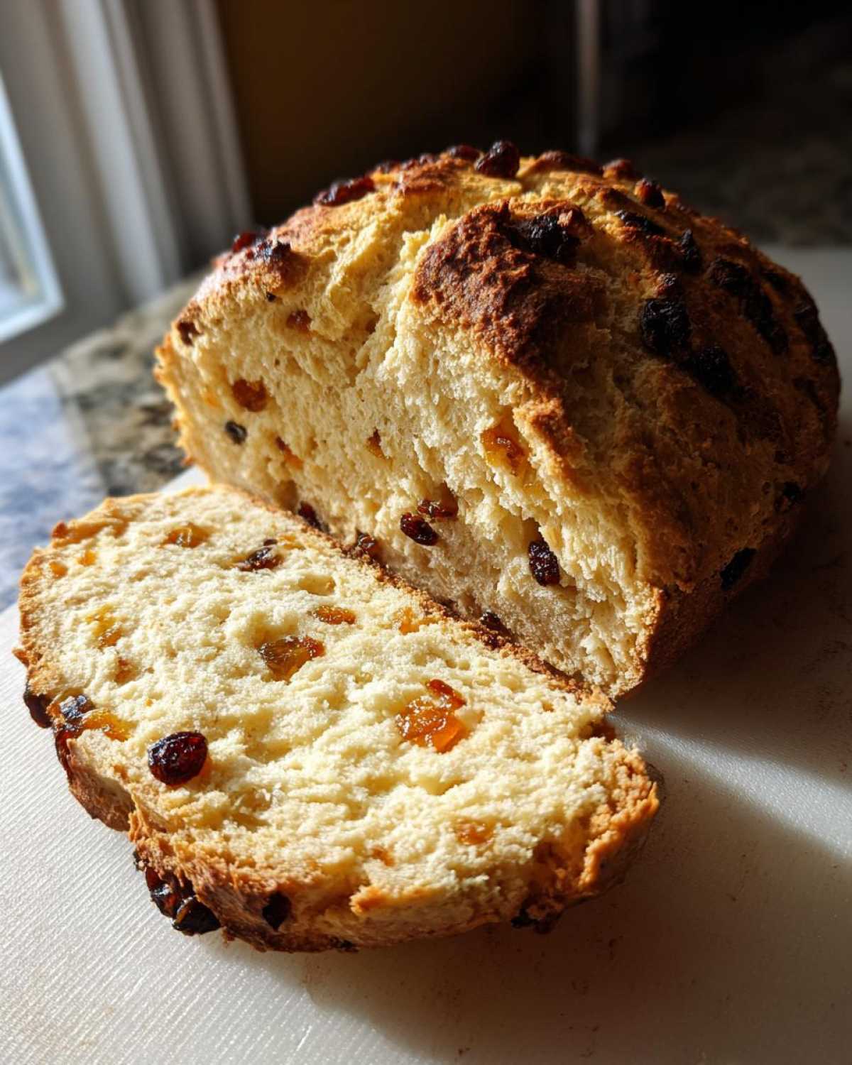A freshly baked loaf of Easy Irish Soda Bread with Buttermilk and Raisins, sliced to show the soft interior texture.