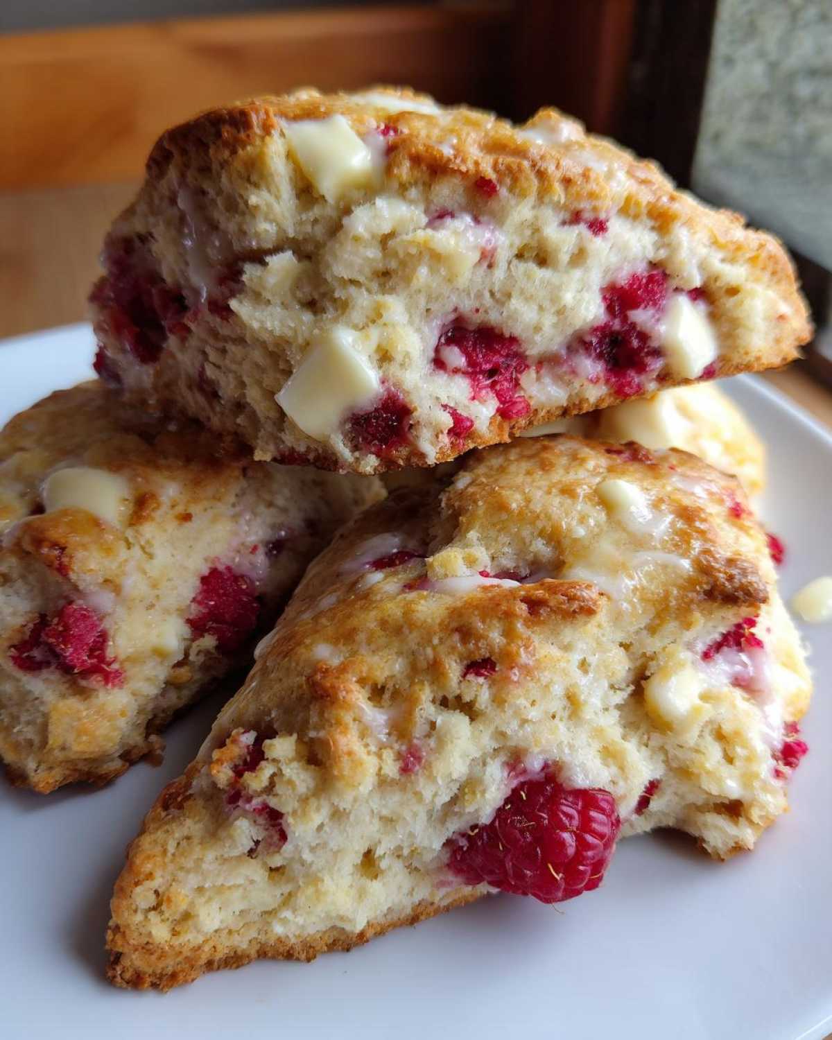 Close-up of flaky White Chocolate Raspberry Scones stacked, showing melted white chocolate chunks and bright red raspberries.