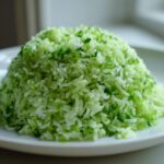 A mound of fluffy, bright green Cilantro Lime Rice served on a white plate.