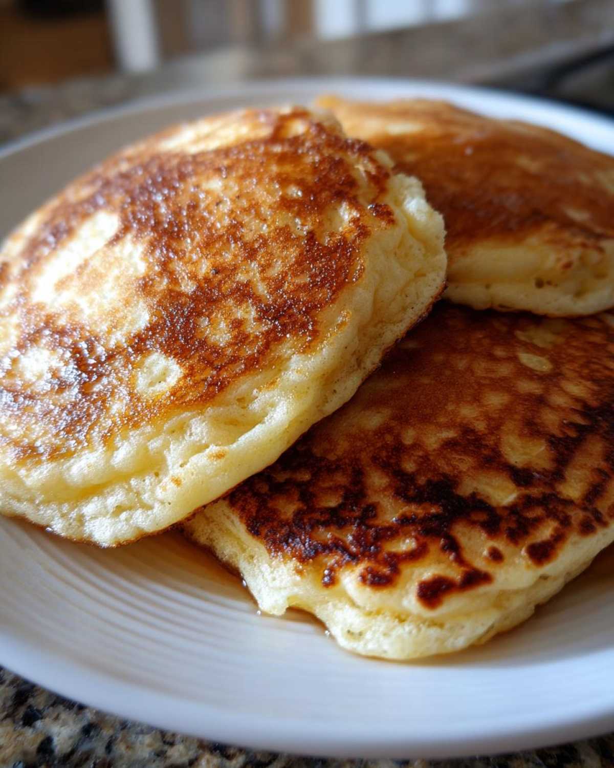 Close-up of three fluffy Gluten-Free Buttermilk Pancakes stacked on a white plate, showing golden-brown, slightly crisp edges.