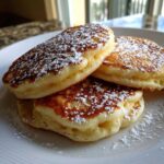 Close-up of three thick, fluffy Lemon Ricotta Pancakes dusted generously with powdered sugar on a white plate.