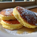 A stack of three incredibly fluffy lemon ricotta pancakes dusted heavily with powdered sugar.