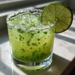 A bright green Fresh Jalapeño Lime Margarita in a rocks glass with a salt rim and lime wheel garnish.