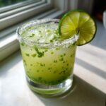 A vibrant Fresh Jalapeño Lime Margarita in a glass with a salt rim and lime wheel garnish.