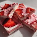 Close-up of broken pieces of Frozen Strawberry Yogurt Bark, showing layers of pink yogurt and fresh strawberry slices.