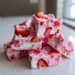 A close-up stack of bright pink and white Frozen Strawberry Yogurt Bark pieces studded with fresh strawberries.