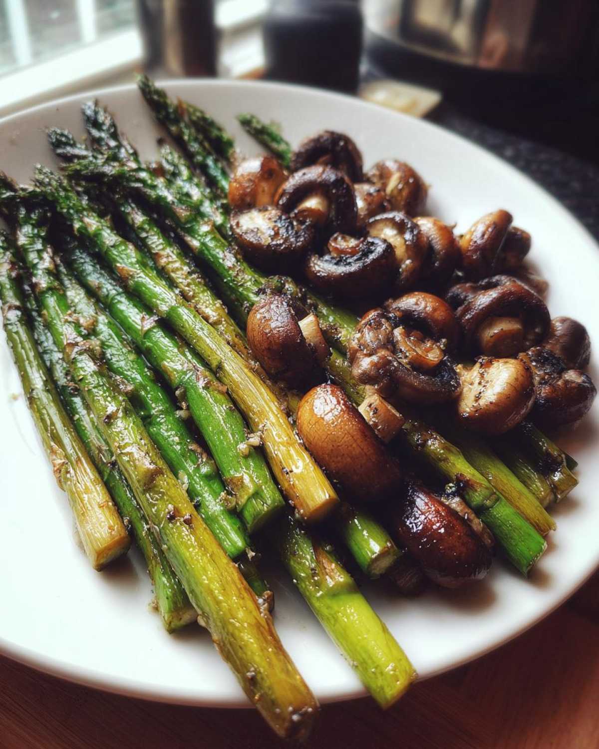 A white plate featuring glossy Garlic Butter Roasted Asparagus and Mushrooms, lightly browned.