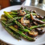 A close-up of perfectly cooked Garlic Butter Roasted Asparagus and Mushrooms on a white plate.