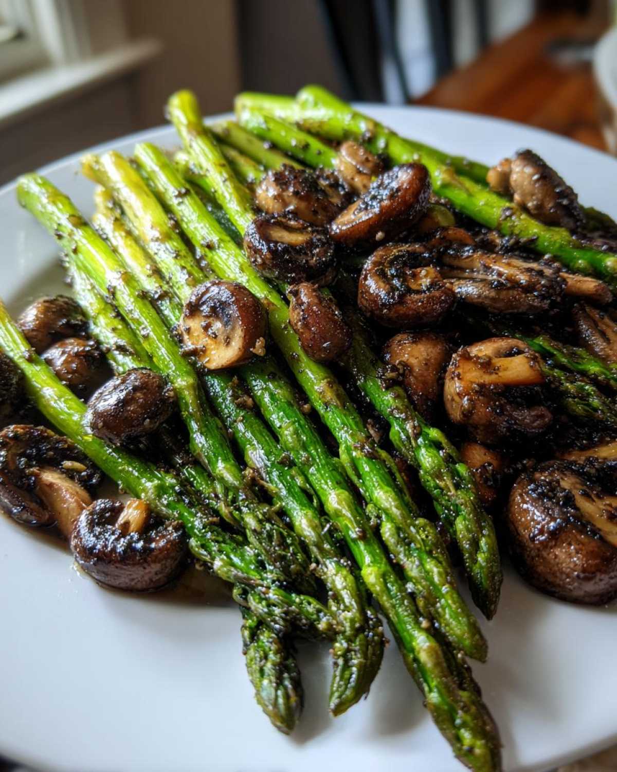 A close-up of vibrant green Garlic Butter Roasted Asparagus and Mushrooms served on a white plate.