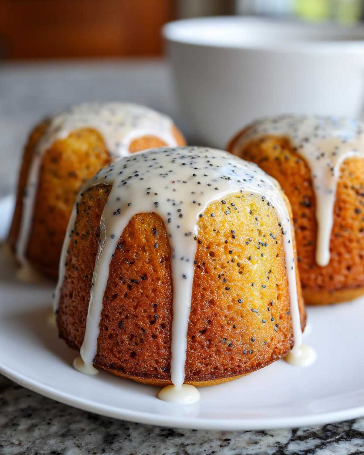 Three golden Glazed Lemon Poppy Seed Muffins topped with thick white lemon icing and visible poppy seeds.