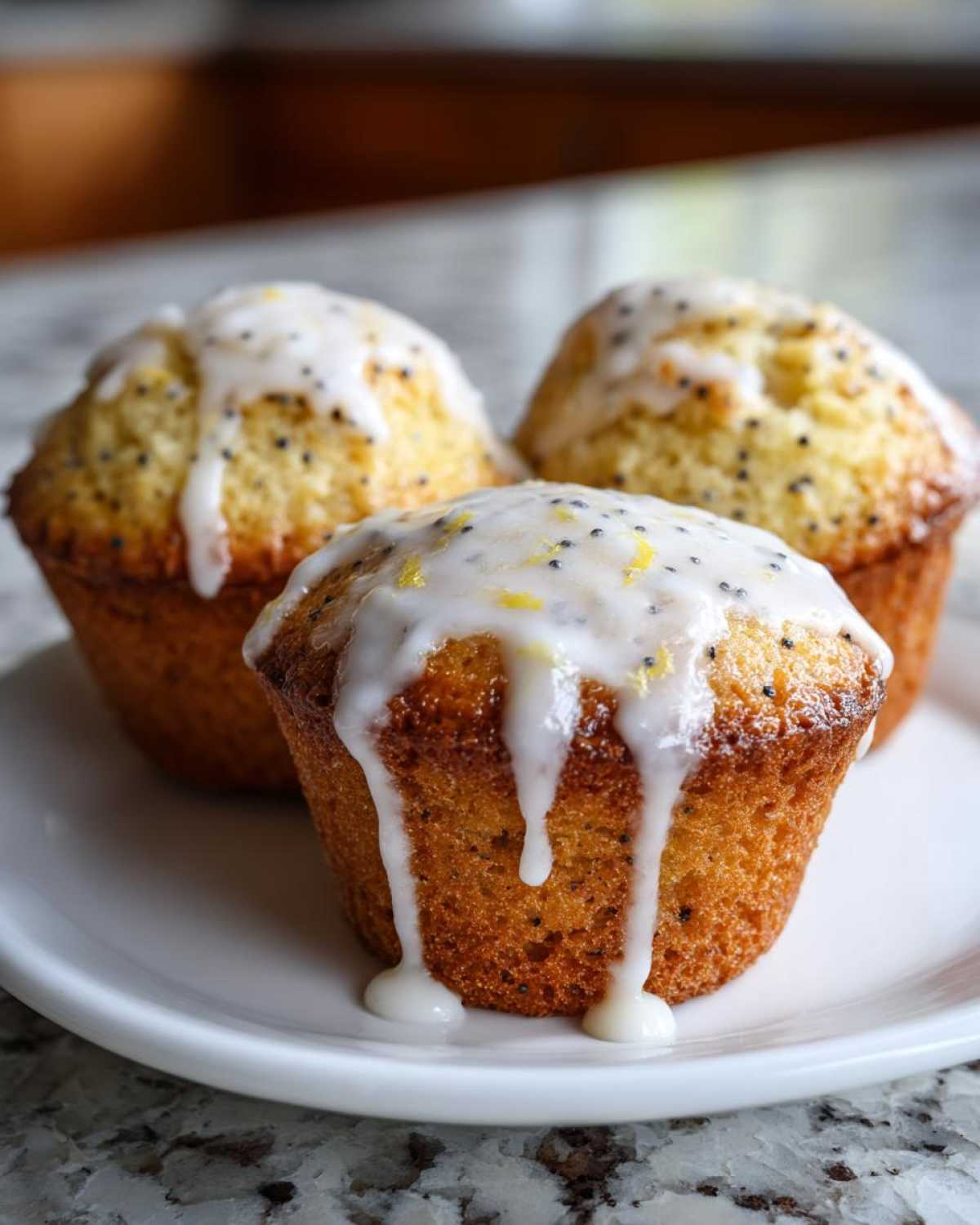 Three freshly baked Glazed Lemon Poppy Seed Muffins topped with thick white icing and lemon zest.