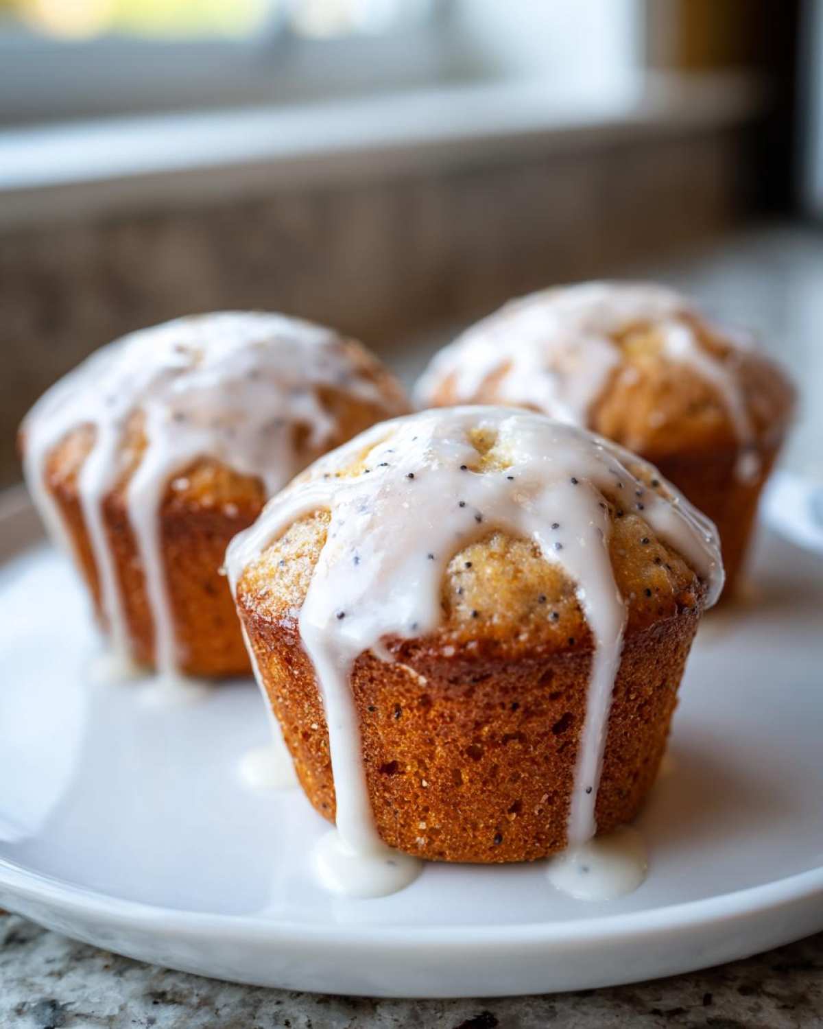 Three golden brown Glazed Lemon Poppy Seed Muffins topped with thick, dripping lemon icing and visible poppy seeds.