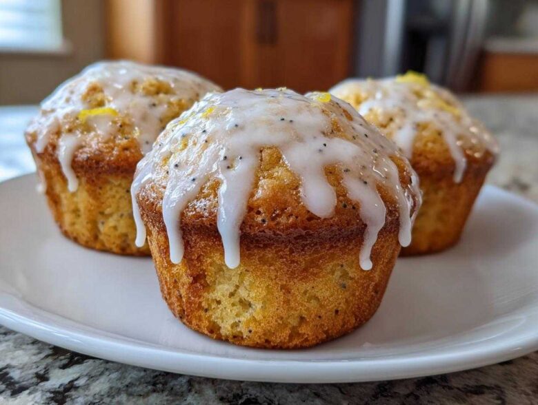 Three freshly baked Glazed Lemon Poppy Seed Muffins with thick white icing dripping down the sides, served on a white plate.